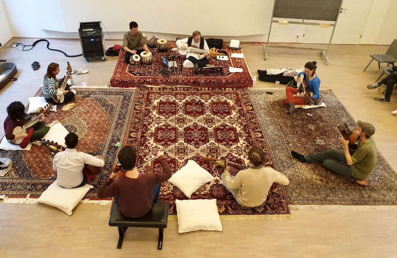 Neun Erwachsene, Männer und Frauen, sitzen im Kreis und spielen indische Instrumente.